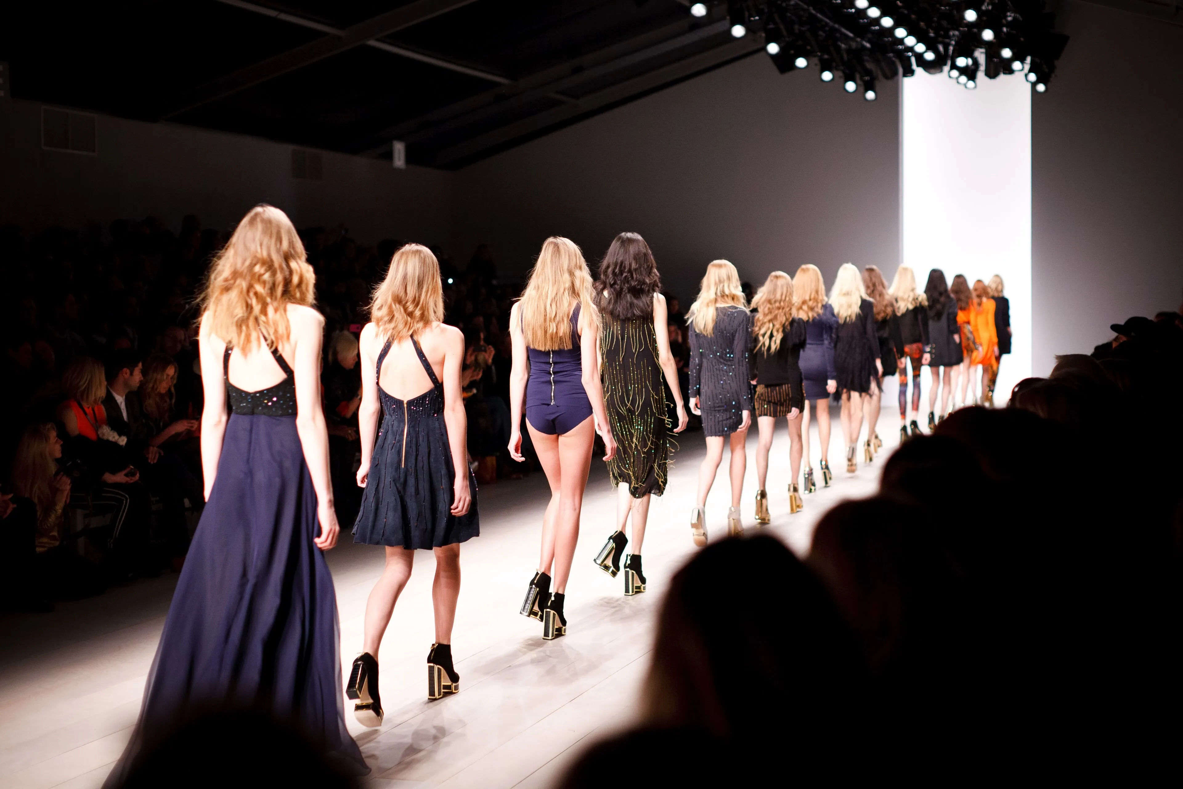 Pasarela, modelos desfilando de espaldas con vestidos oscuros